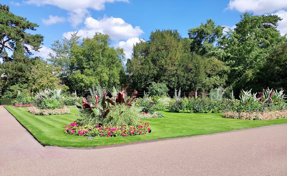 A vibrant garden scene featuring an array of flowering plants and ornamental grasses arranged in neat beds. In the foreground, a cluster of purple petunias with delicate, ruffled petals are planted ar